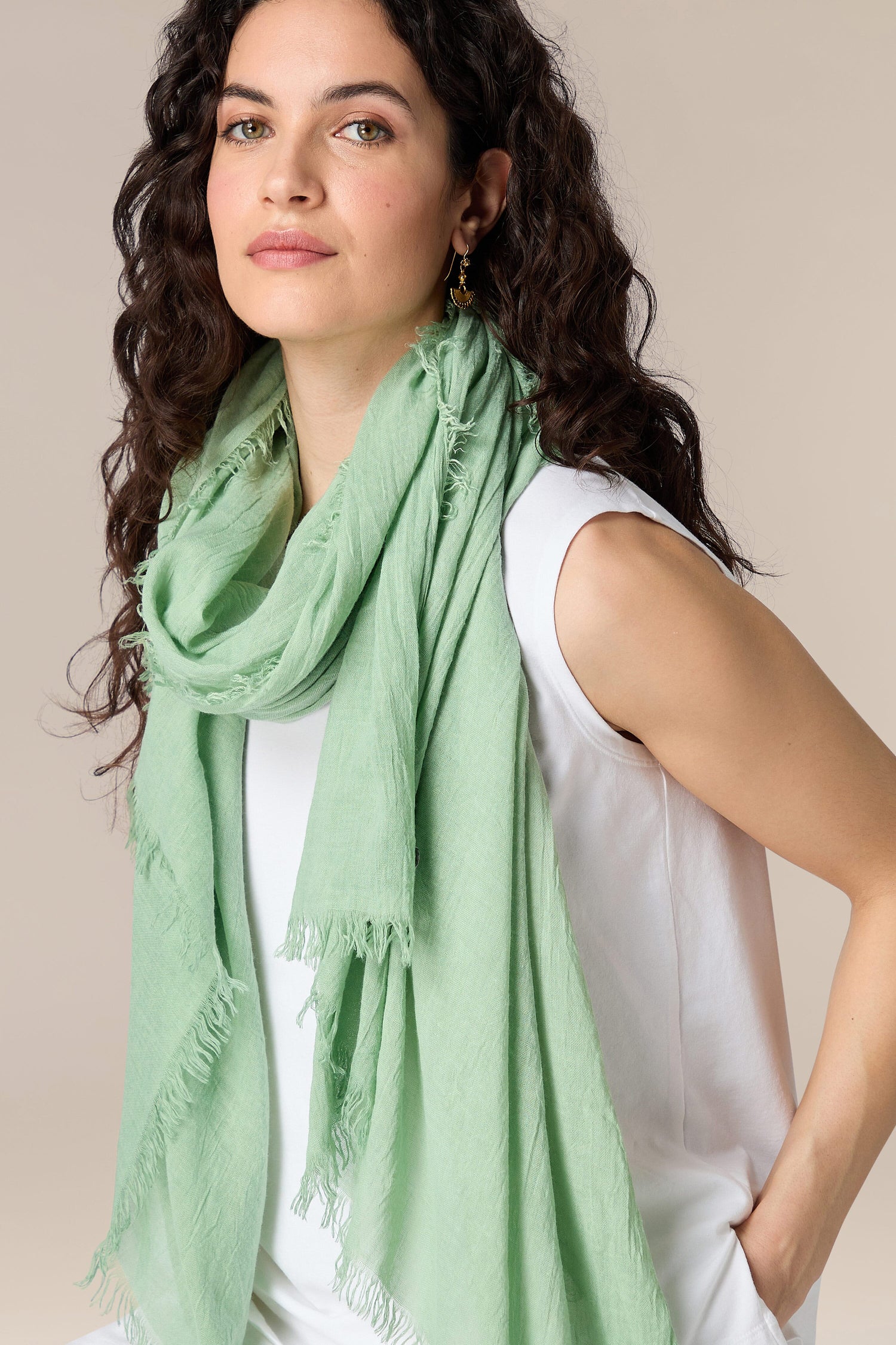 A woman with curly hair wearing a white sleeveless top and a light green Soft Fringe Scarf.