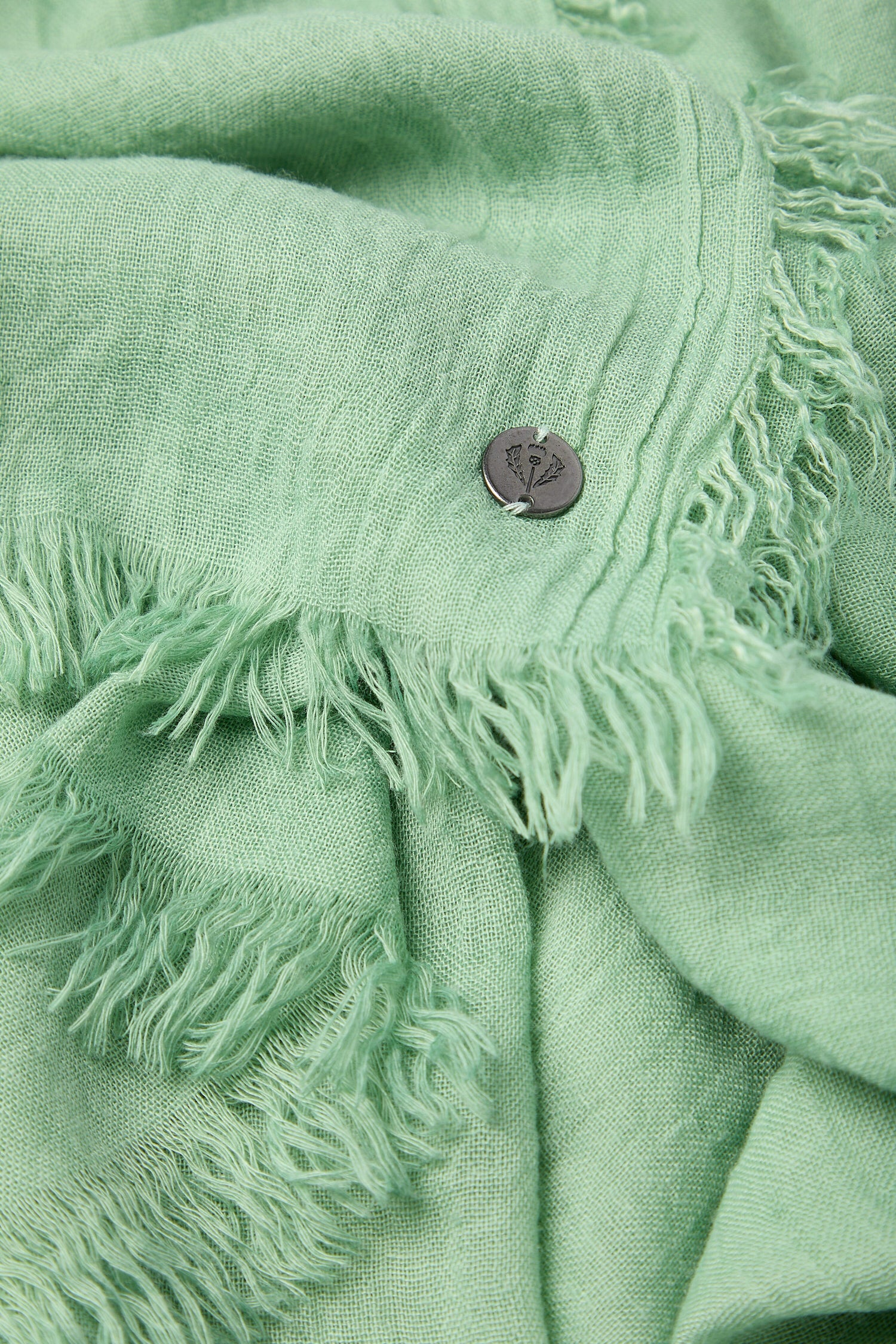 Close-up of a green textured Soft Fringe Scarf with soft fringe edges and a button, offering versatile styling options.