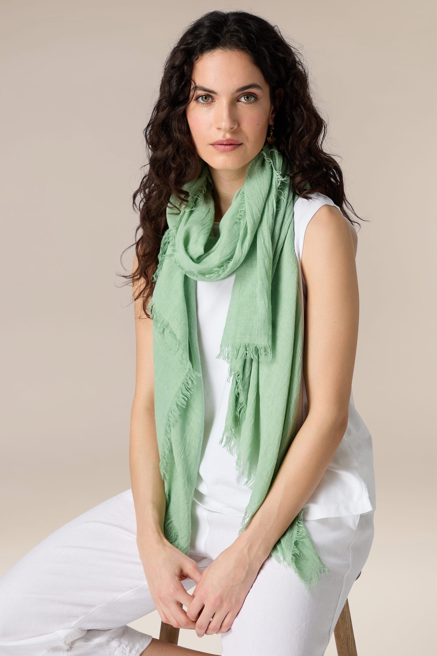 Woman sitting on a stool wearing a white outfit with a Soft Fringe Scarf.