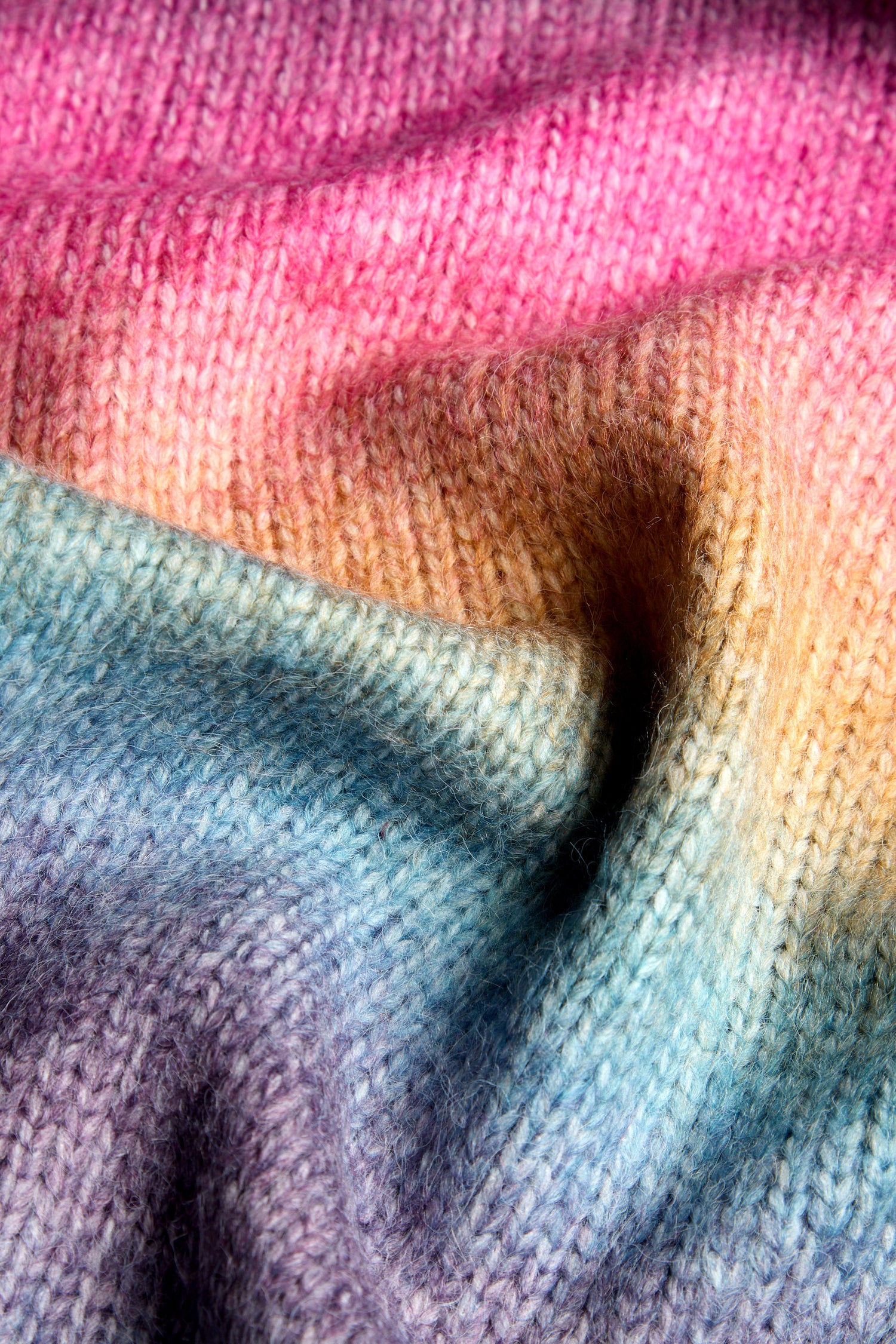 Close-up of the Rainbow Stripe Knit Scarf, highlighting a gradient of colors that transition from pink and orange at the top to blue and purple at the bottom. This cozy accessory features rainbow stripes seamlessly integrated into its vibrant design.