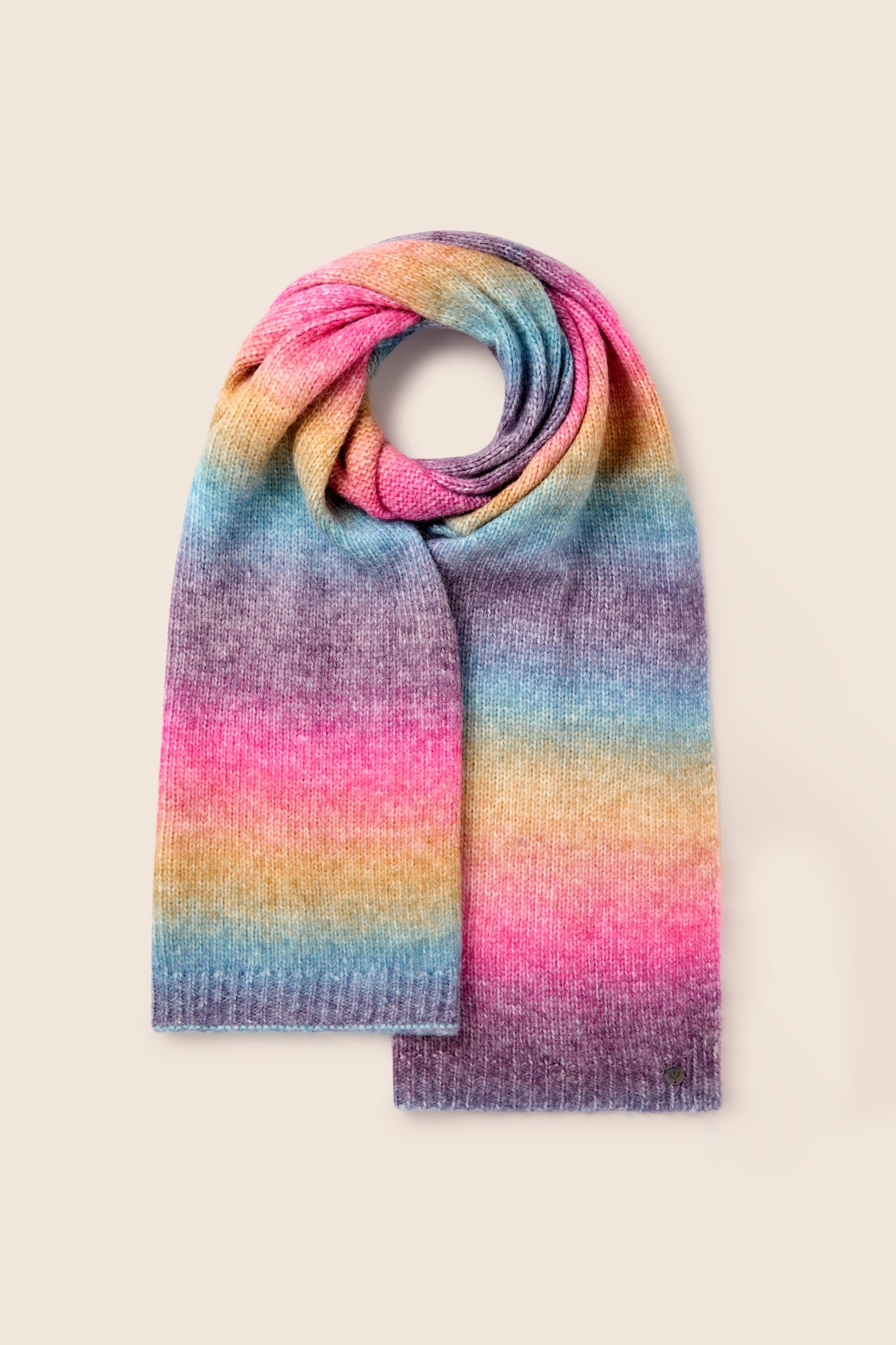 The Rainbow Stripe Knit Scarf is a cozy accessory adorned with horizontal rainbow stripes in shades of pink, purple, yellow, green, and blue against a beige backdrop.