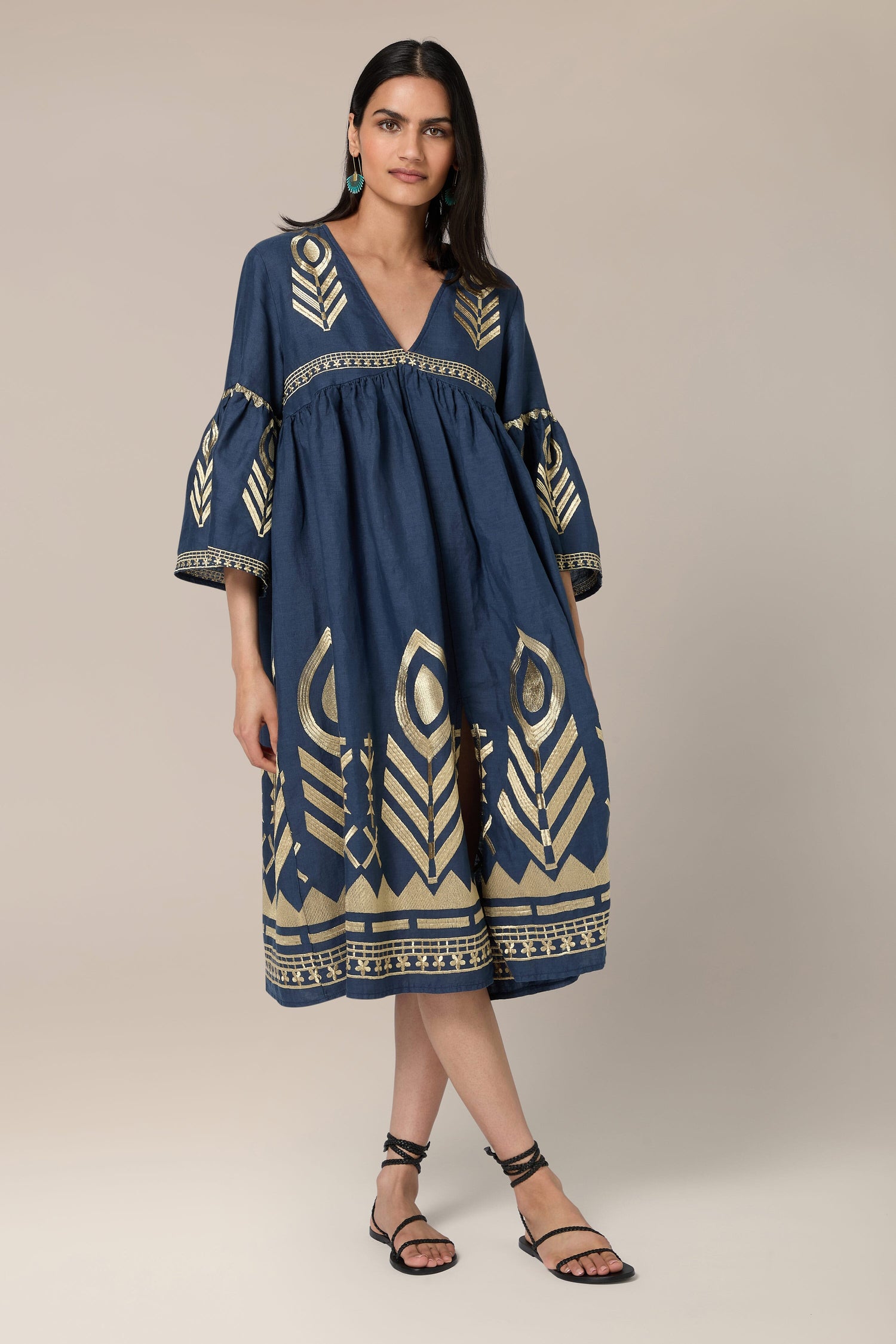 Woman wearing the Feathers Linen Midi Dress, long sleeves, and black strappy sandals, standing against a beige background.