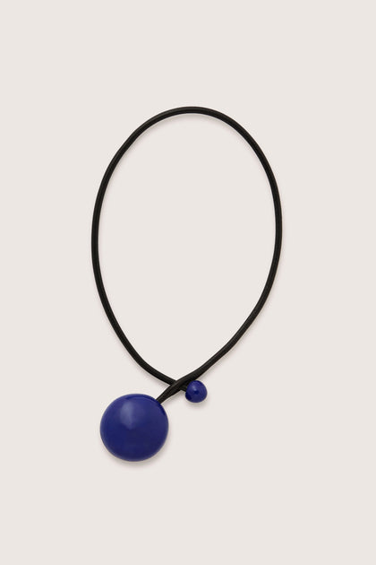 The Handmade Ceramic Bead Necklace features a black cord adorned with two blue ceramic bead pendants of varying sizes, one large and one small, exemplifying contemporary French craftsmanship.