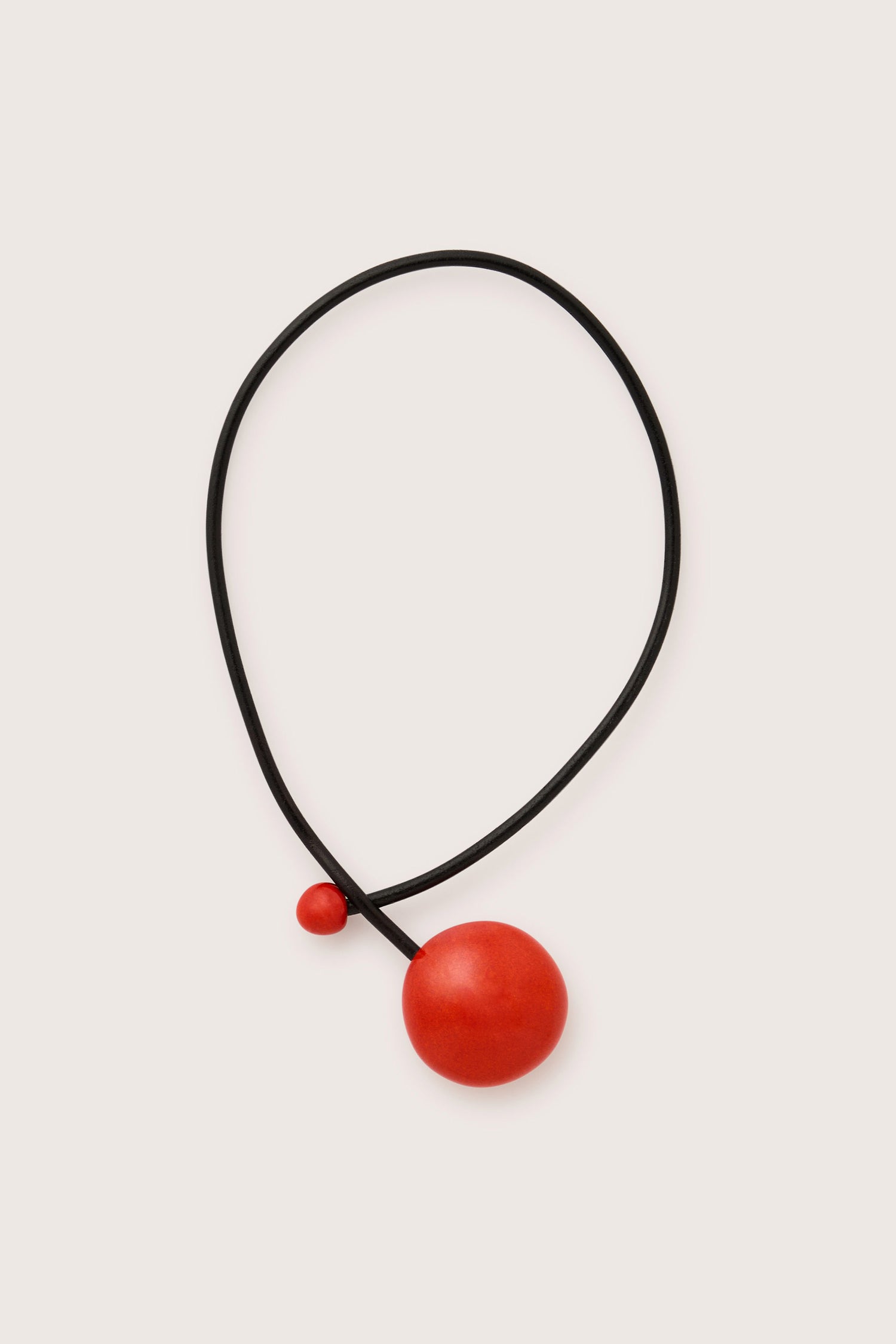 Introducing the Handmade Ceramic Bead Necklace - a black cord necklace adorned with two red, handcrafted ceramic beads. The beads, one large and one small, are arranged asymmetrically to enhance its modern aesthetic. This piece showcases exquisite French craftsmanship and boasts a contemporary design.