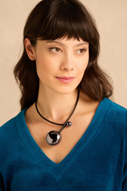 A person wearing a Handmade Charcoal Ceramic Bead Necklace featuring two dark, spherical beads on a black leather cord.