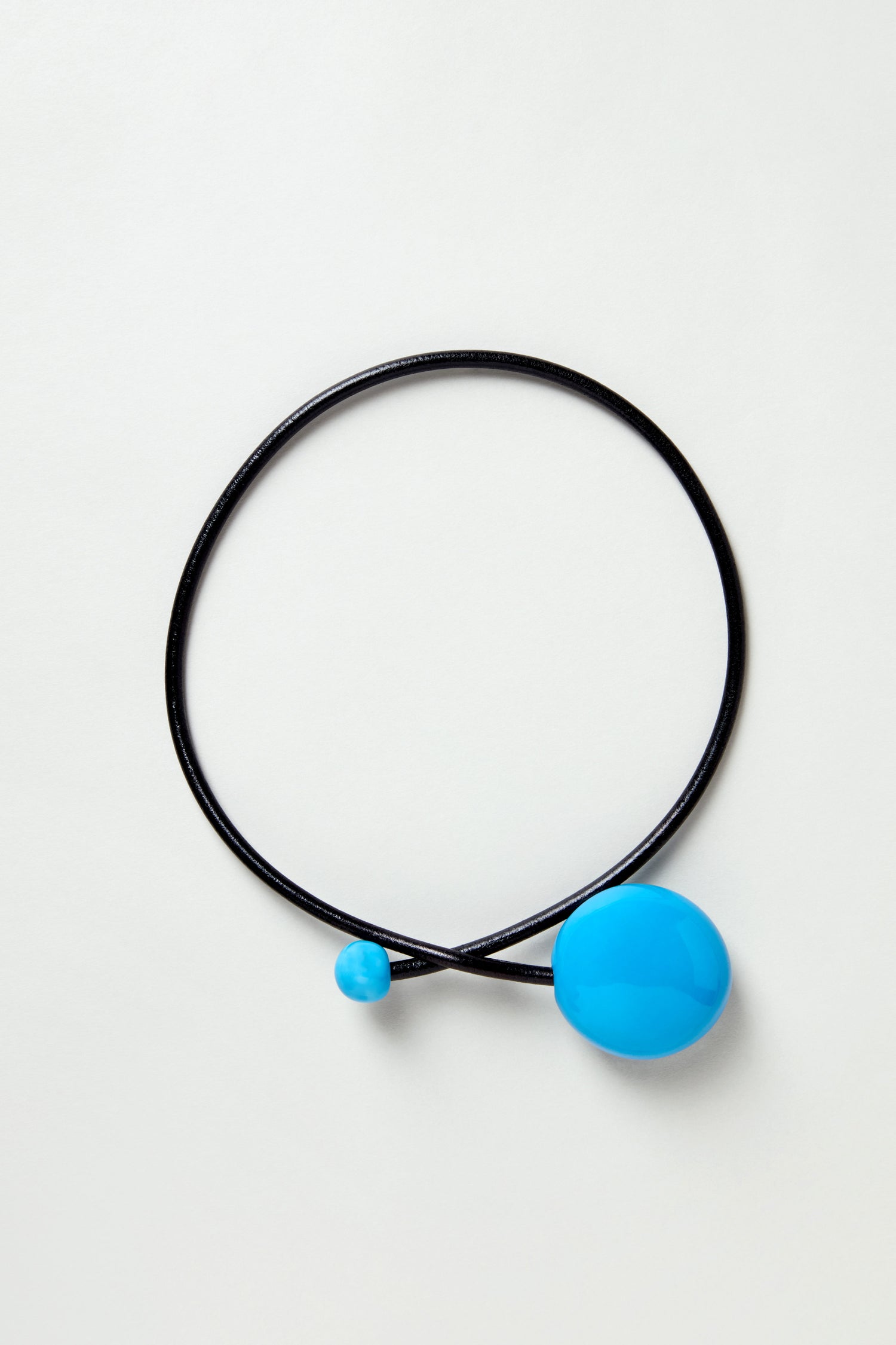 The Handmade Ceramic Bead Necklace features two blue oval ceramic beads, one large and one small, strung on a black cord and displayed against a plain light background.