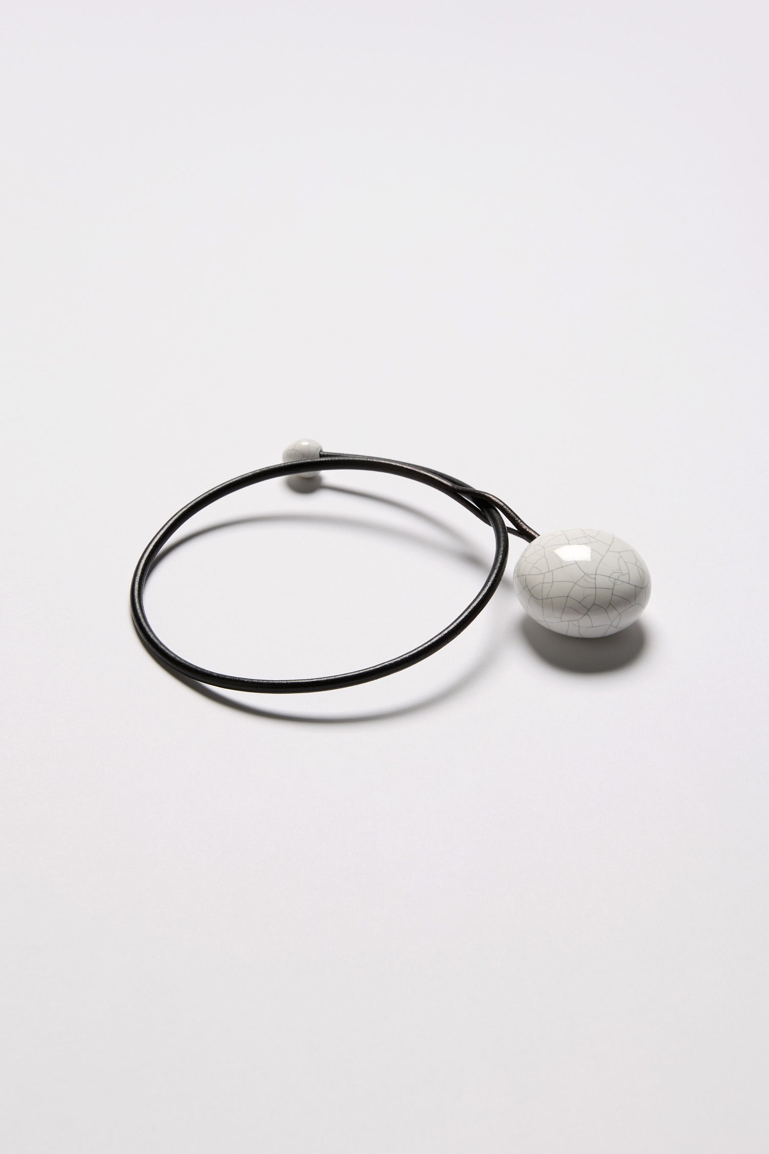 The Handmade Ceramic Crackle Bead Necklace features two white Gevole ceramic beads, one large and one small, on a minimalist black bracelet and is displayed on a plain white background.