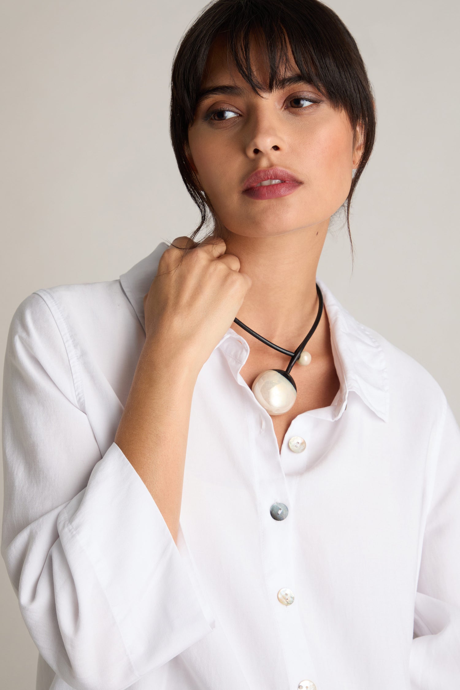 Woman wearing a white button-up shirt and a Handmade Ceramic Pearl Bead Necklace featuring two large pearl-like ceramic beads, looking slightly to the side with a neutral expression.