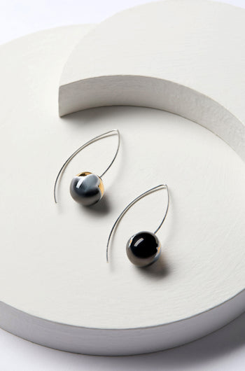 Discover the elegance of our Handmade Ceramic Graphic Earrings, featuring a pair of modern minimalist style earrings adorned with round black and silver beads. These earrings are beautifully displayed on a light, textured circular surface, making them perfect for those who appreciate geometric ceramic shapes.