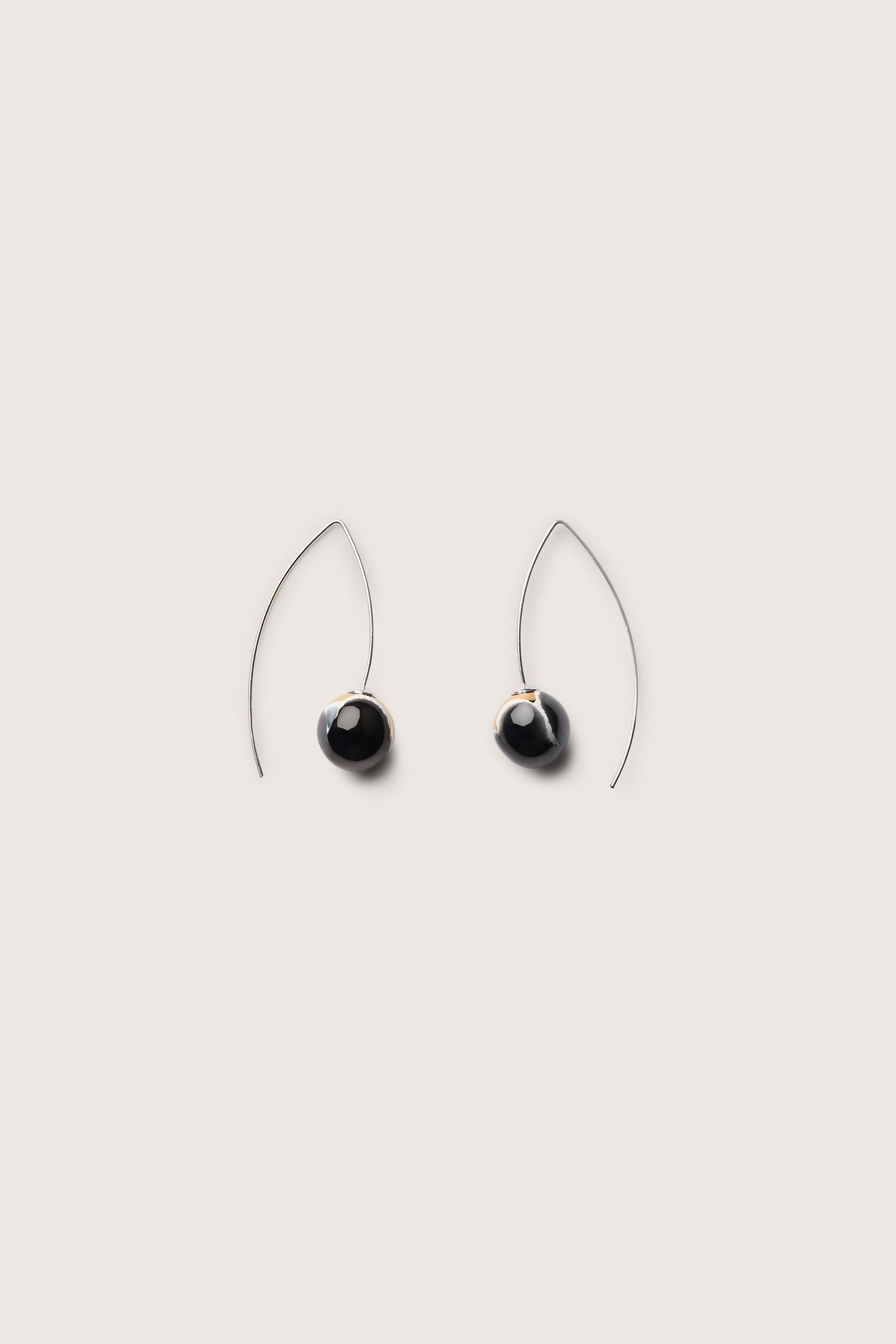 A pair of handmade ceramic graphic earrings featuring a modern minimalist teardrop shape with black stones and thin, curved wire hooks against a plain background.