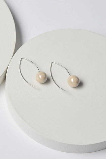 Handmade Ceramic Bead Earrings with minimalist design, featuring wooden spherical beads and curved 925 sterling silver wires, showcasing artisanal craftsmanship, placed on a white circular surface.