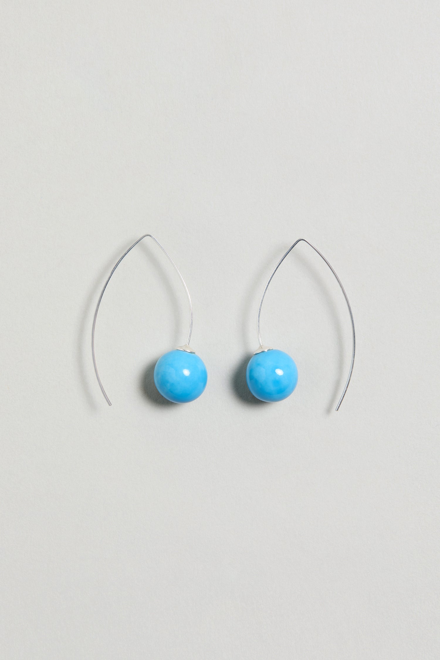 Handmade Ceramic Bead Earrings with silver hooks feature round, bright turquoise ceramic beads and are displayed on a light gray background. These earrings add a vibrant touch to any outfit.