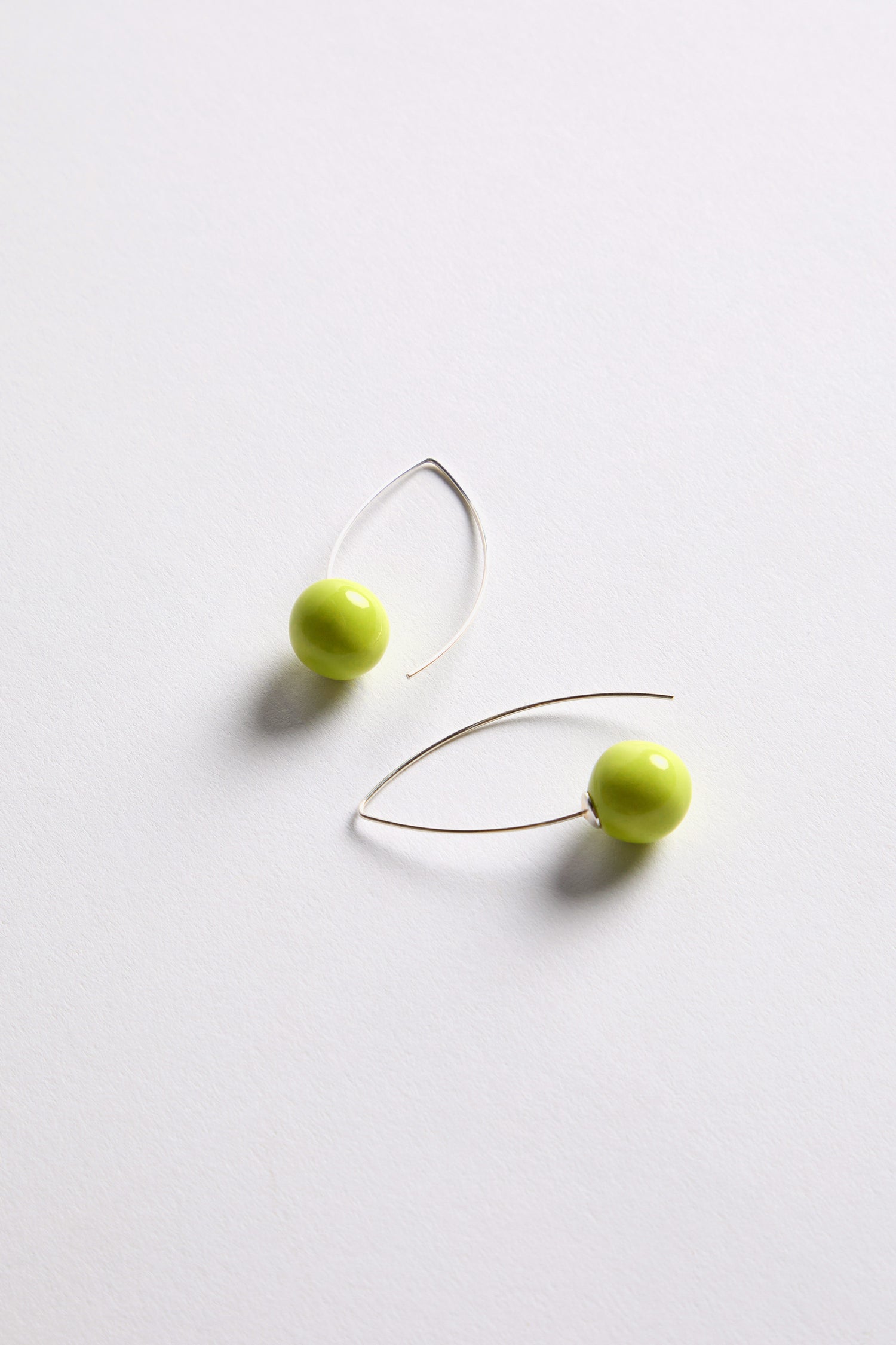 Handmade Ceramic Bead Earrings: Sculptural silver wire earrings with a round lime green bead, showcased on a plain white surface.