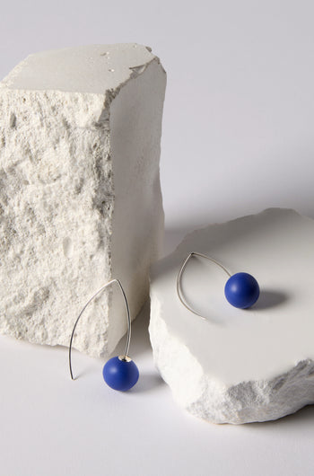 Handmade Ceramic Bead Earrings with blue spheres and an organic finish, shown on two rough white stone blocks.