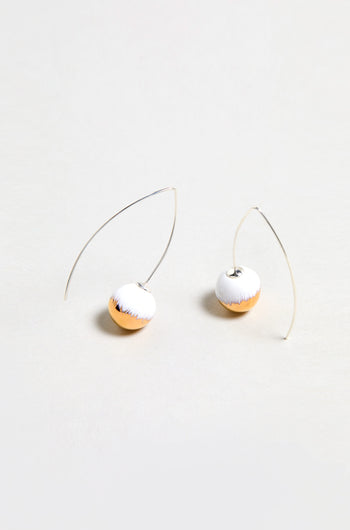 Handmade Gold Brushstroke Ceramic Bead Earrings feature curved silver wires and round, half-white, half-gold ceramic beads. Inspired by gold brushstroke earrings and photographed on a plain light background.