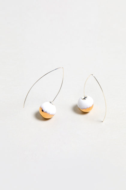 Handmade Gold Brushstroke Ceramic Bead Earrings feature curved silver wires and round, half-white, half-gold ceramic beads. Inspired by gold brushstroke earrings and photographed on a plain light background.