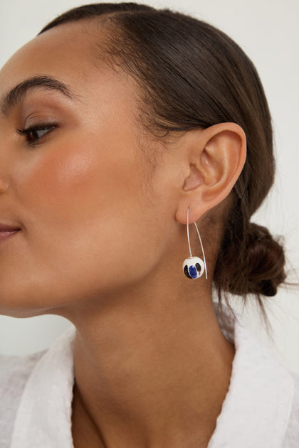 Close-up of a person wearing Handmade Painted Ceramic Bead Earrings with a blue and white circular design, featuring smooth skin and neatly tied hair.