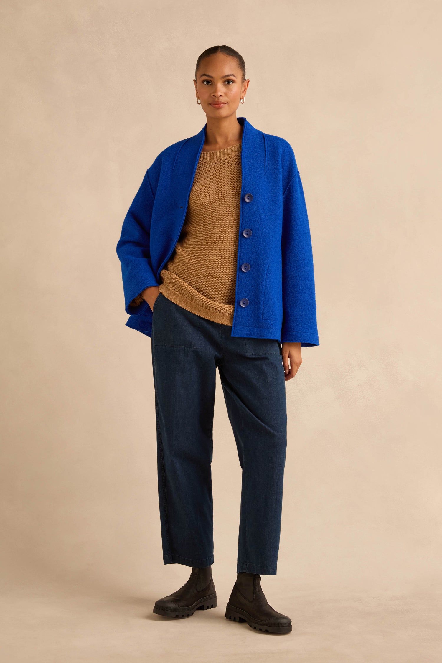 A person wearing a Cobalt Boiled Wool Cocoon jacket in cobalt blue over a tan sweater and dark blue trousers.