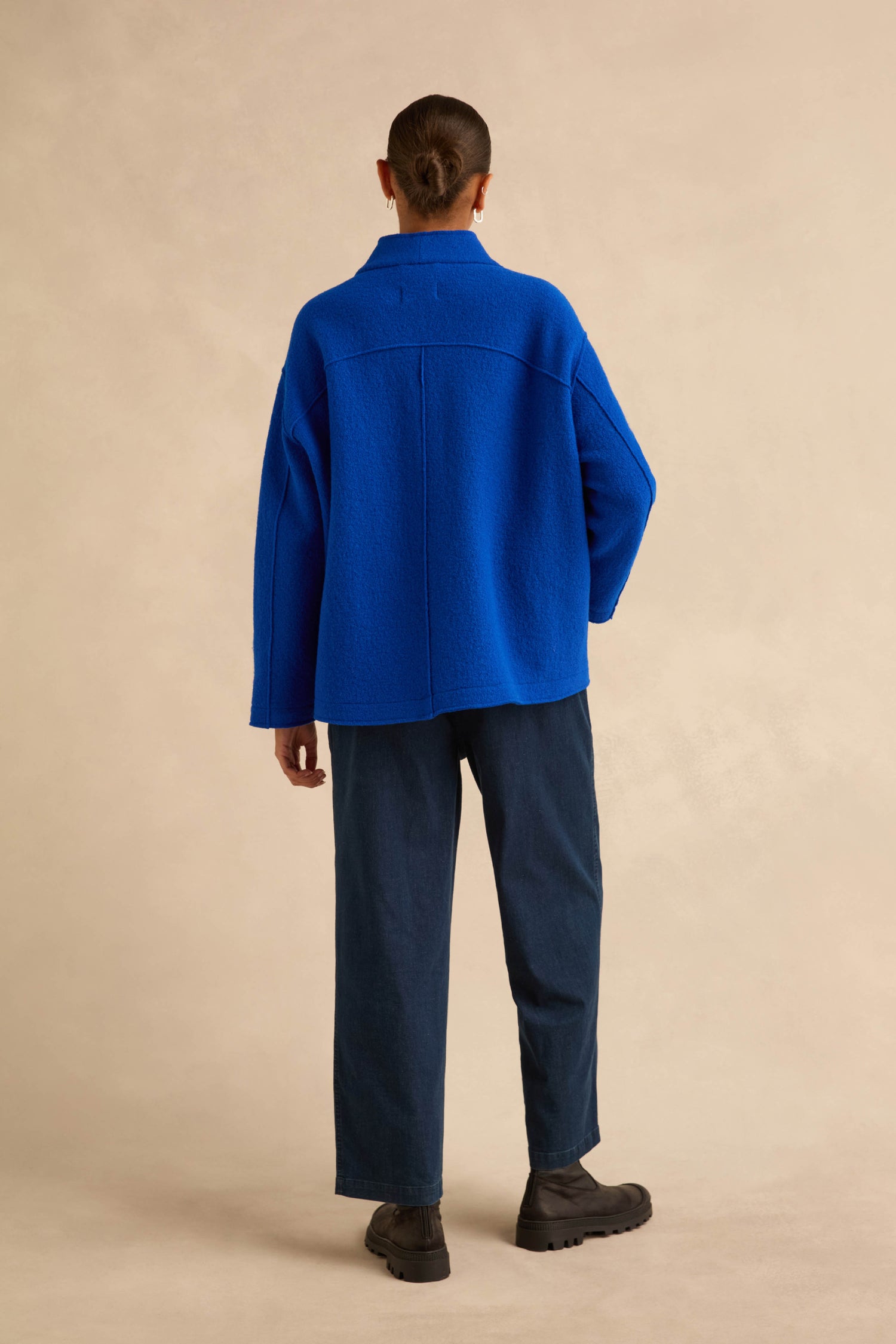 A person seen from behind wearing a Cobalt Boiled Wool Cocoon Jacket, dark trousers, and black ankle boots.