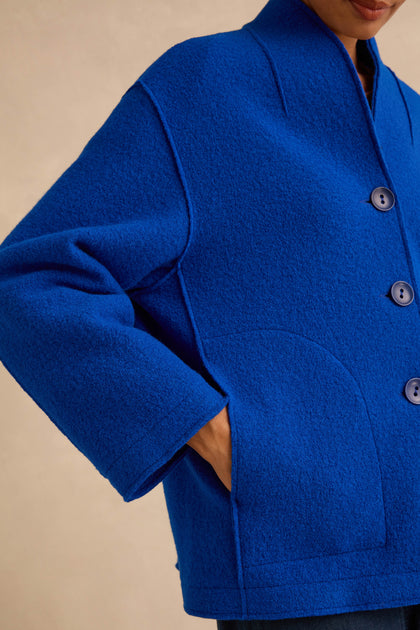 A person wearing a cobalt blue Cobalt Boiled Wool Cocoon Jacket with patch pockets and a stand collar.