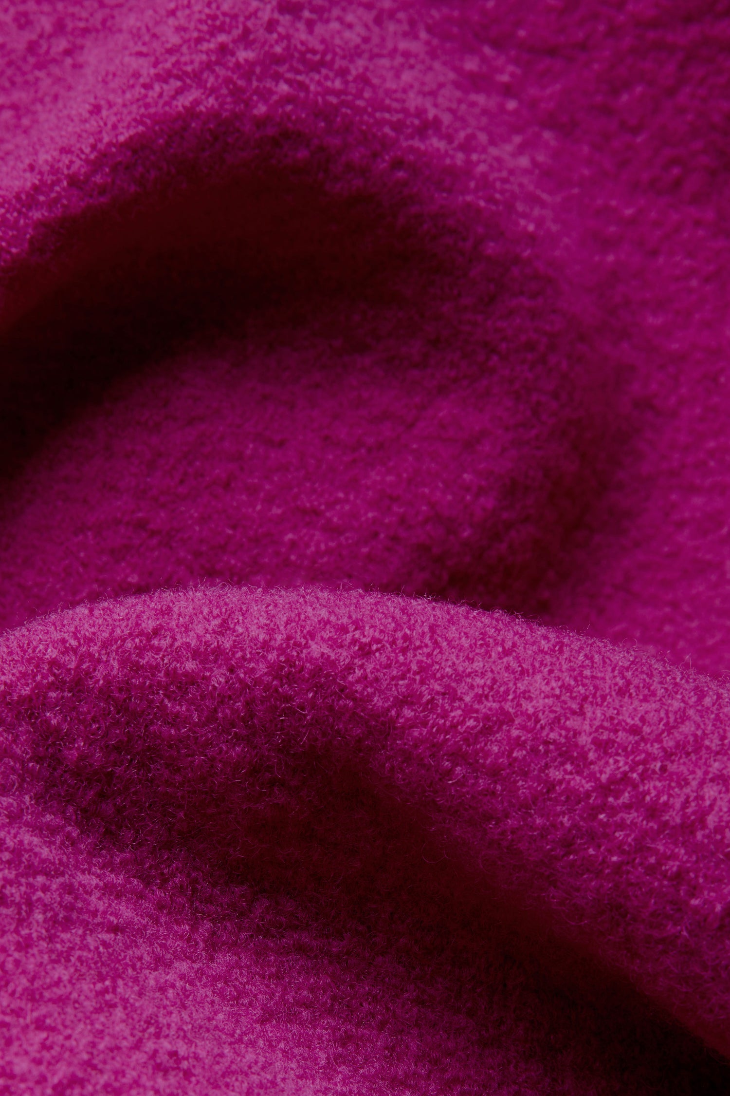 Close-up of the textured magenta fabric of the Magenta Boiled Wool Cocoon Jacket, with visible fibers and soft folds, reminiscent of traditional English craftsmanship.