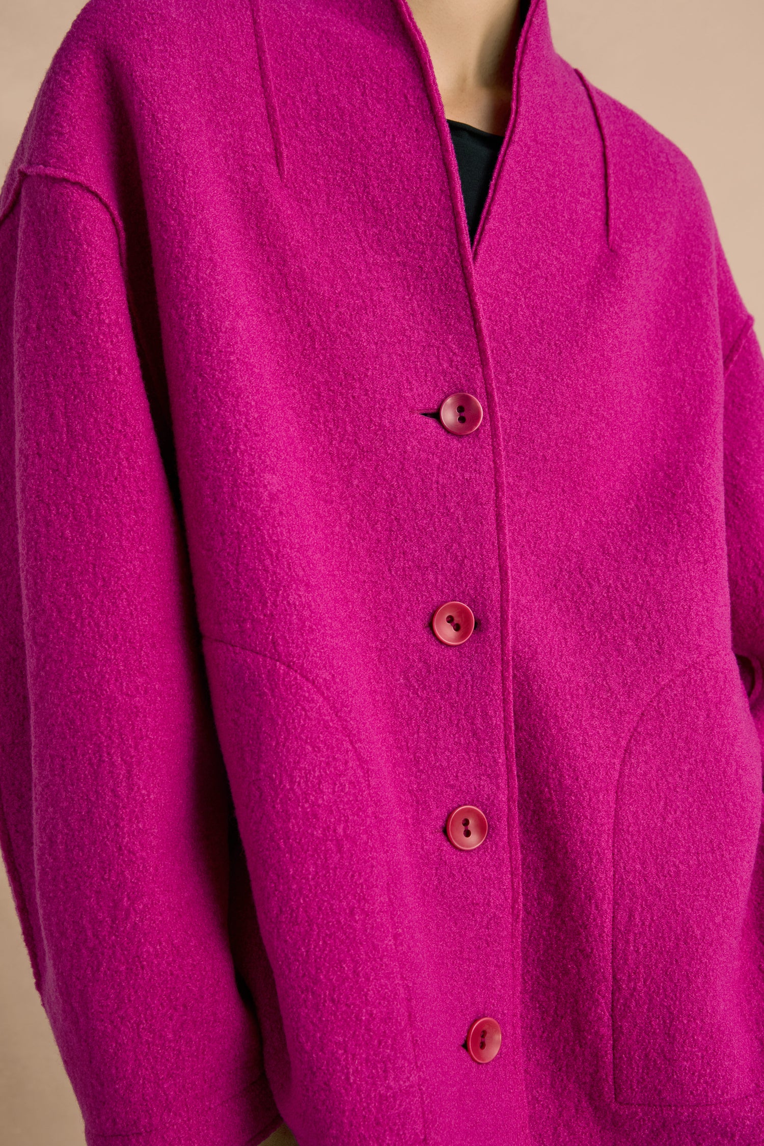 Person wearing the Magenta Boiled Wool Cocoon Jacket, a bright pink jacket with a high collar and side pockets, featuring a cocoon silhouette, photographed from the shoulders to the waist.