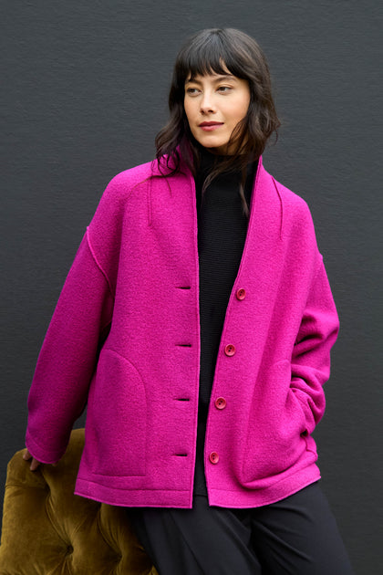 A woman wearing a Magenta Boiled Wool Cocoon Jacket in a magenta, cocoon-silhouette boiled wool over a black turtleneck.