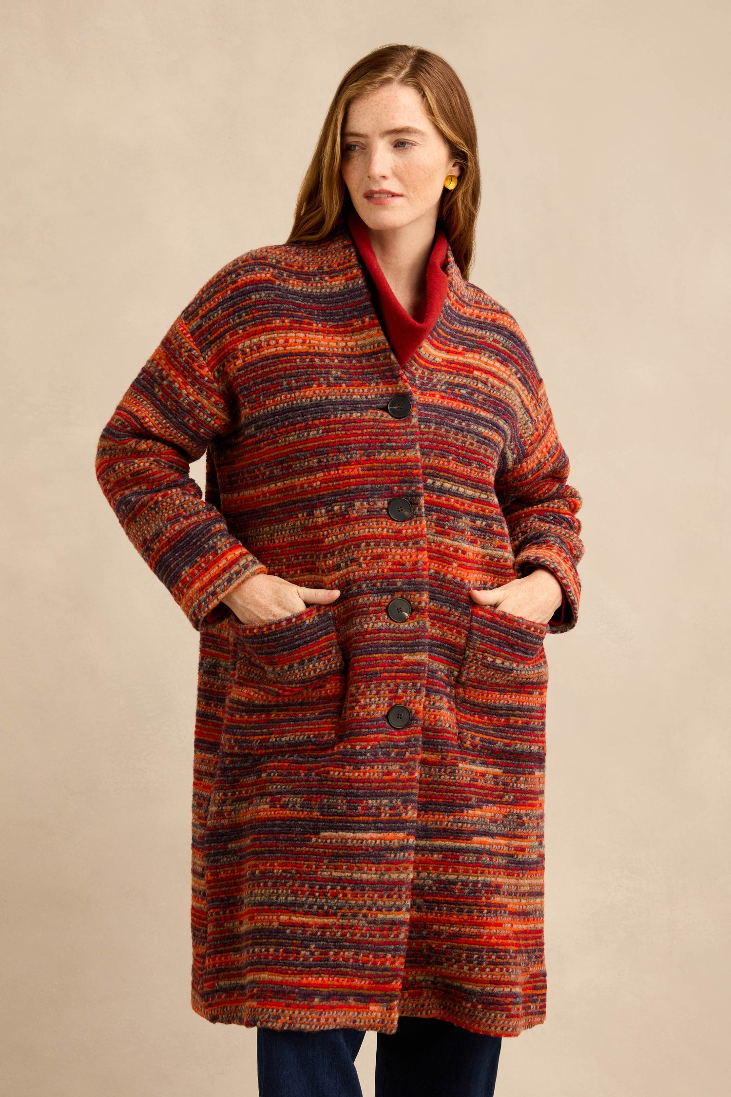 A woman wears the Artisan Wool Blend Stripe Coat—a long, multicolored piece featuring large buttons and front pockets. She stands with her hands tucked into the pockets, gazing slightly to the side.