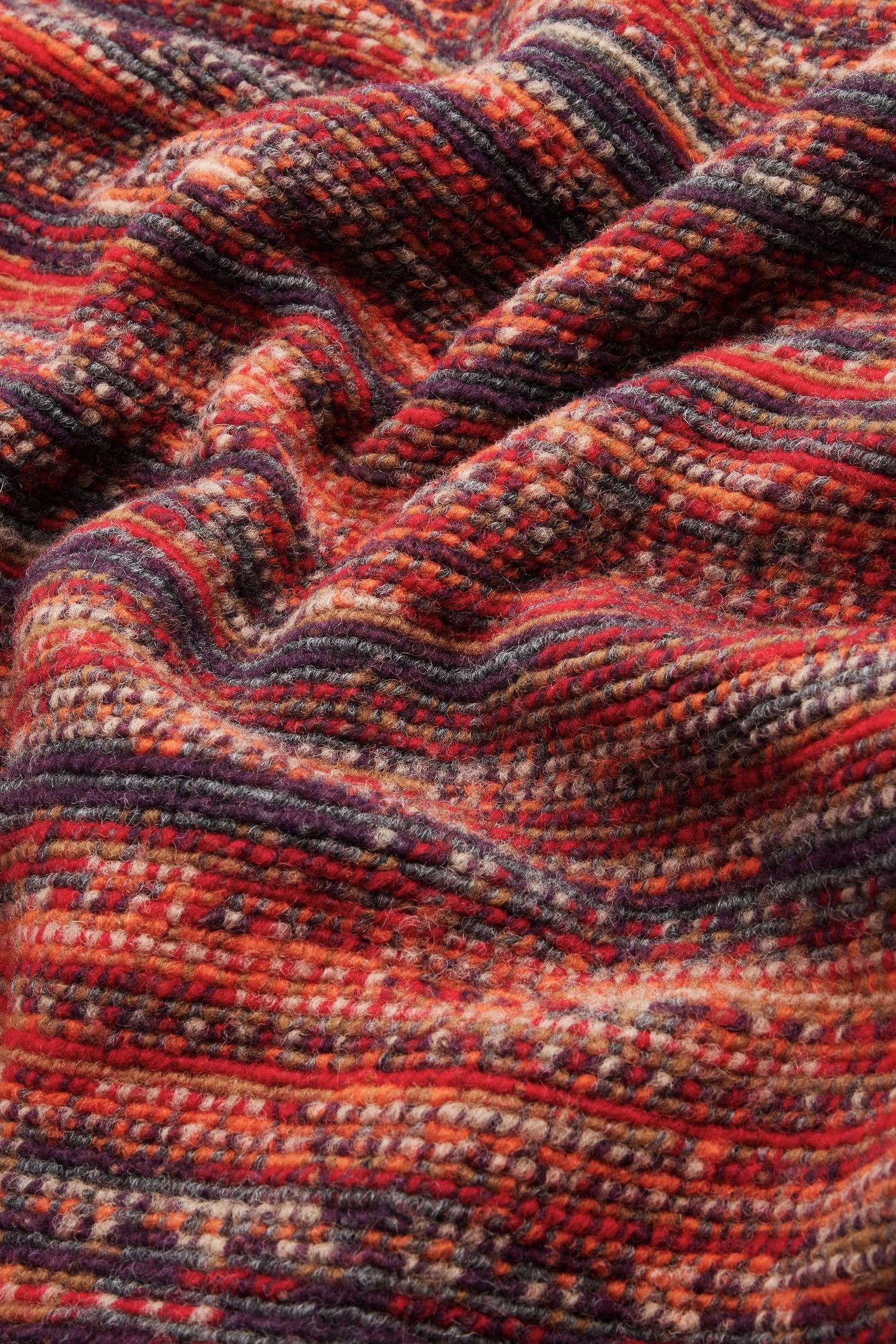 Close-up of textured fabric with red, orange, purple, and beige horizontal stripes, showing folds and a soft, woven appearance—perfect for the Artisan Wool Blend Stripe Coat or an oversized stripe coat.