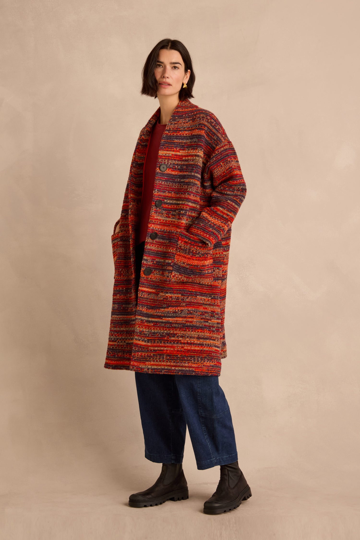 A woman stands against a beige background, wearing the Artisan Wool Blend Stripe Coat over a red shirt, blue jeans, and black boots.