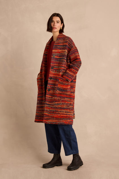A woman stands against a beige background, wearing the Artisan Wool Blend Stripe Coat over a red shirt, blue jeans, and black boots.