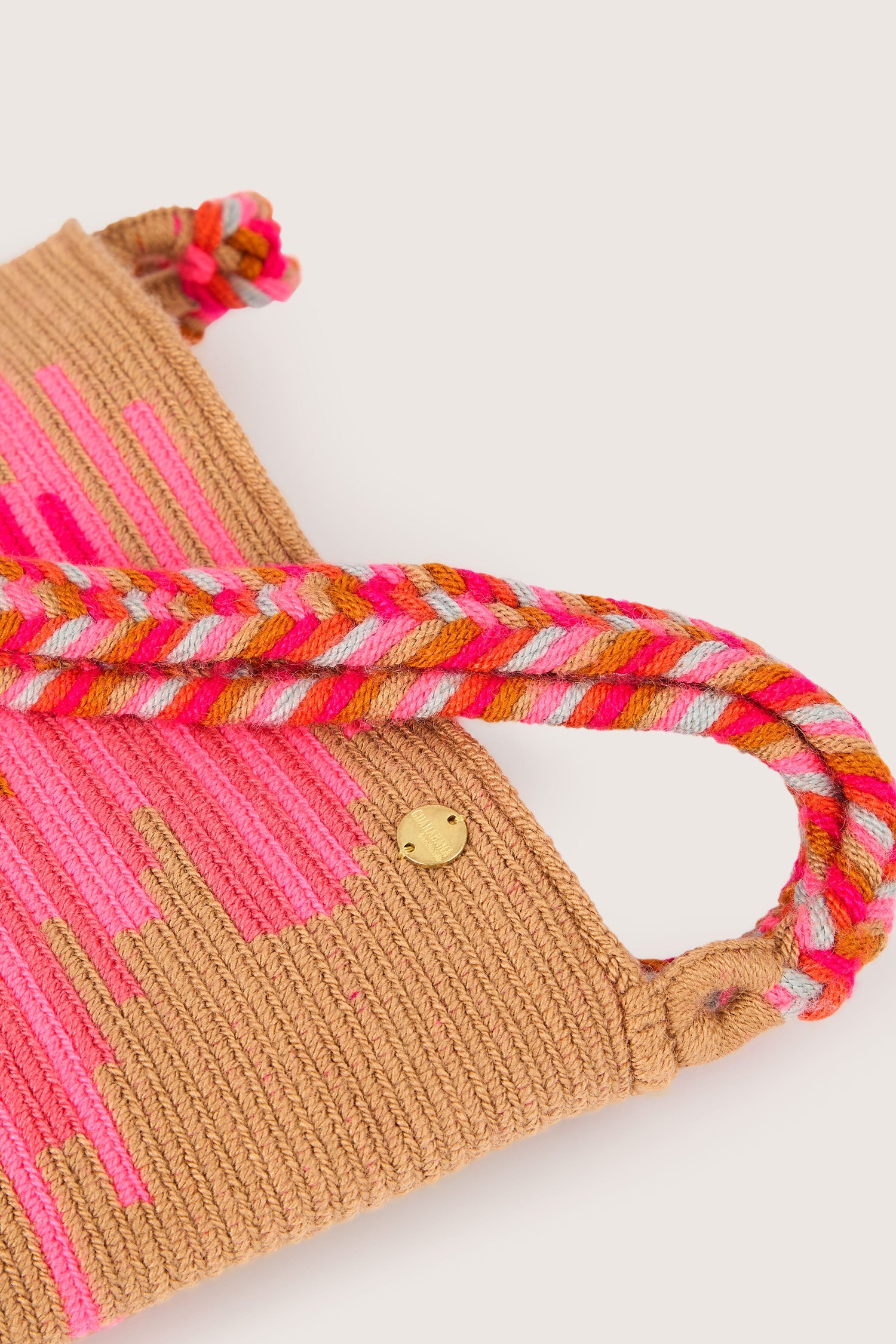 A close-up of the Handcrafted Rectangular Crossbody Bag reveals pink and beige patterns. Featuring a twisted multicolored handle and a small round metal clasp, this bag is handcrafted by skilled artisans, showcasing vibrant colors and playful patterns.