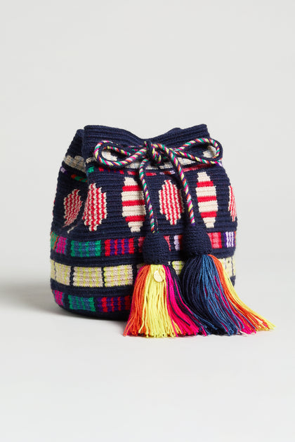 The Hand Crocheted Wayuu Geometric Crossbody Bag showcases colorful geometric patterns, two large multicolored tassels, and a woven drawstring design on a white background.