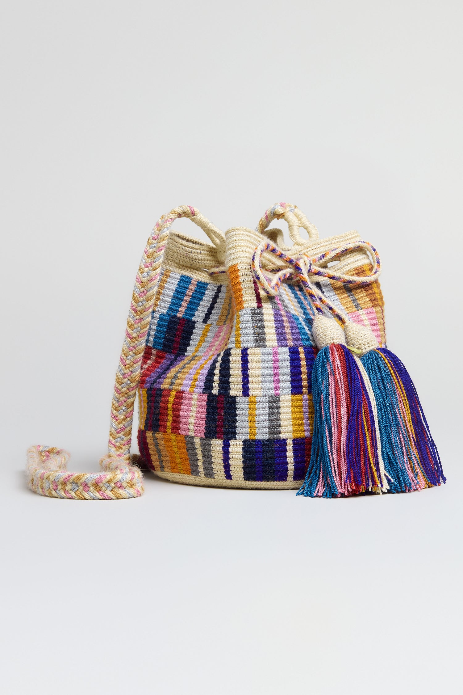 The Hand Crocheted Wayuu Crossbody Bag features a multicoloured geometric design, braided shoulder strap, and large tassel, displayed on a plain white background.