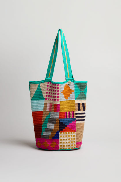 The Hand Crocheted Cala Tote Bag features a vibrant geometric design in multiple colors with a green handle, shown against a plain white background.