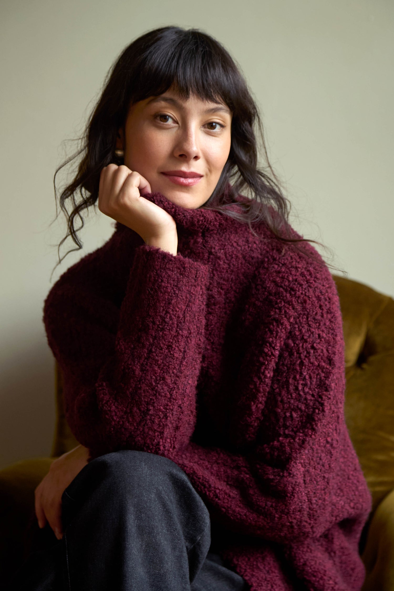 A woman wearing a dark red Bordeaux Boucle Cable Knit Jumper with a cable knit texture.