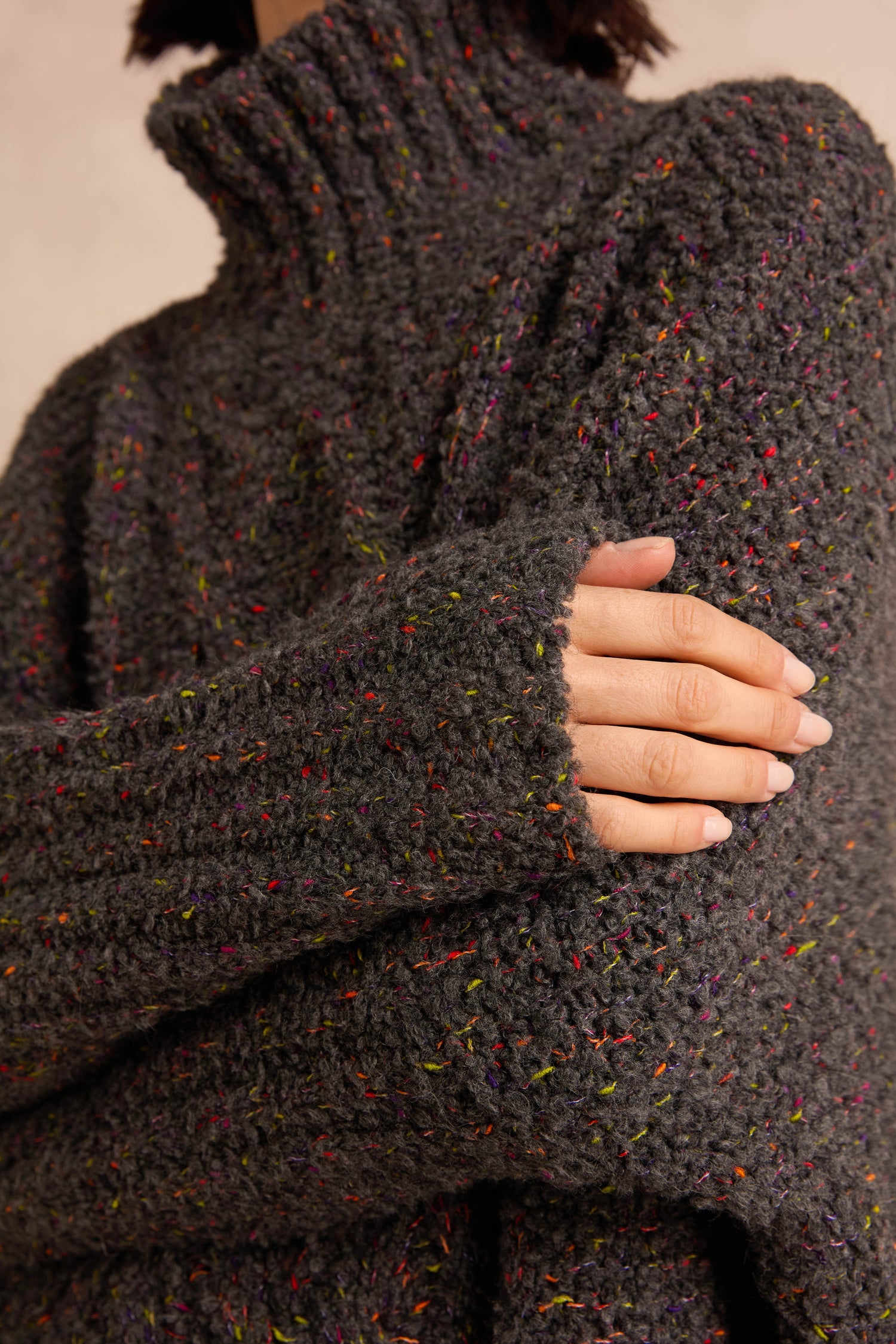A person wearing the Graphite Boucle Cable Knit Jumper, with their hand resting on their upper arm, highlights the soft, textured Italian-made sweater.
