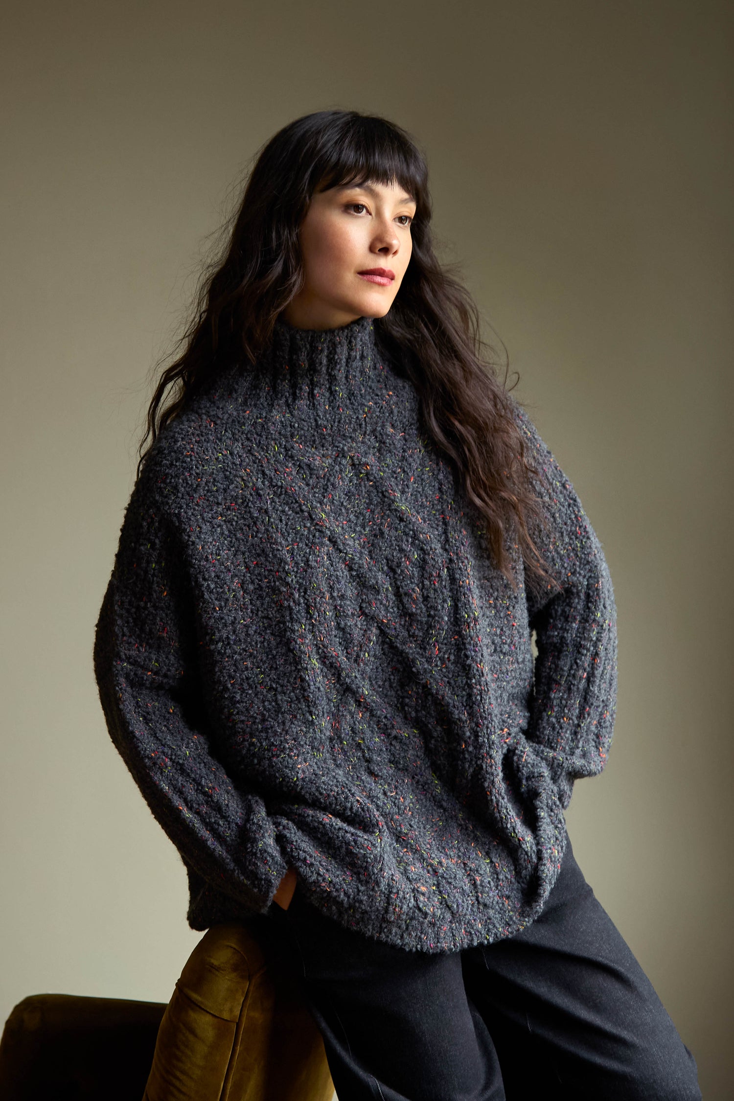 A Graphite Boucle Cable Knit Jumper in charcoal grey, featuring a cable-knit texture with multicolored flecks and a mock neckline, made in Italy.