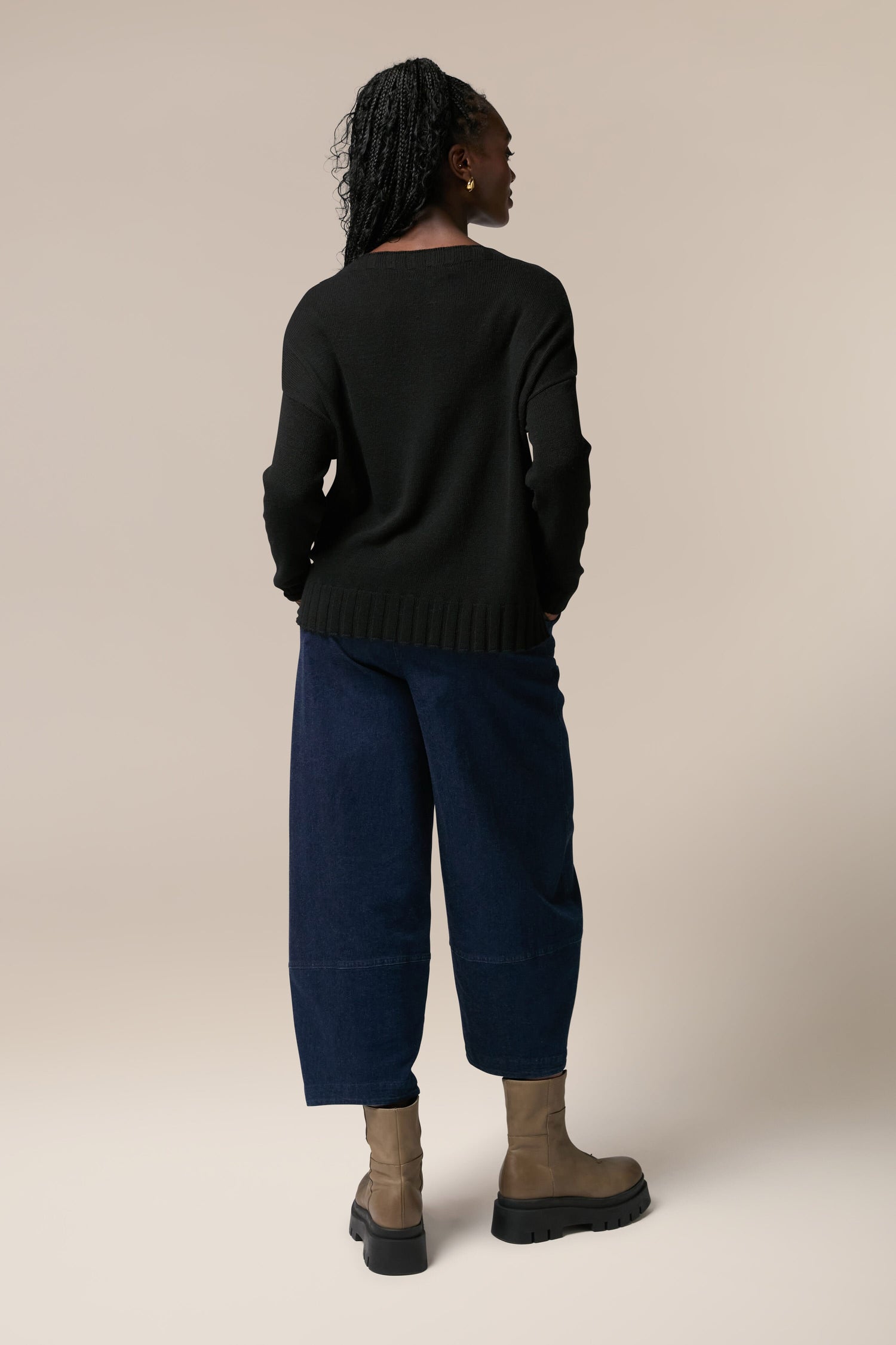 The back view of a woman wearing a black Cashmere Merino Crop Jumper and blue pants.