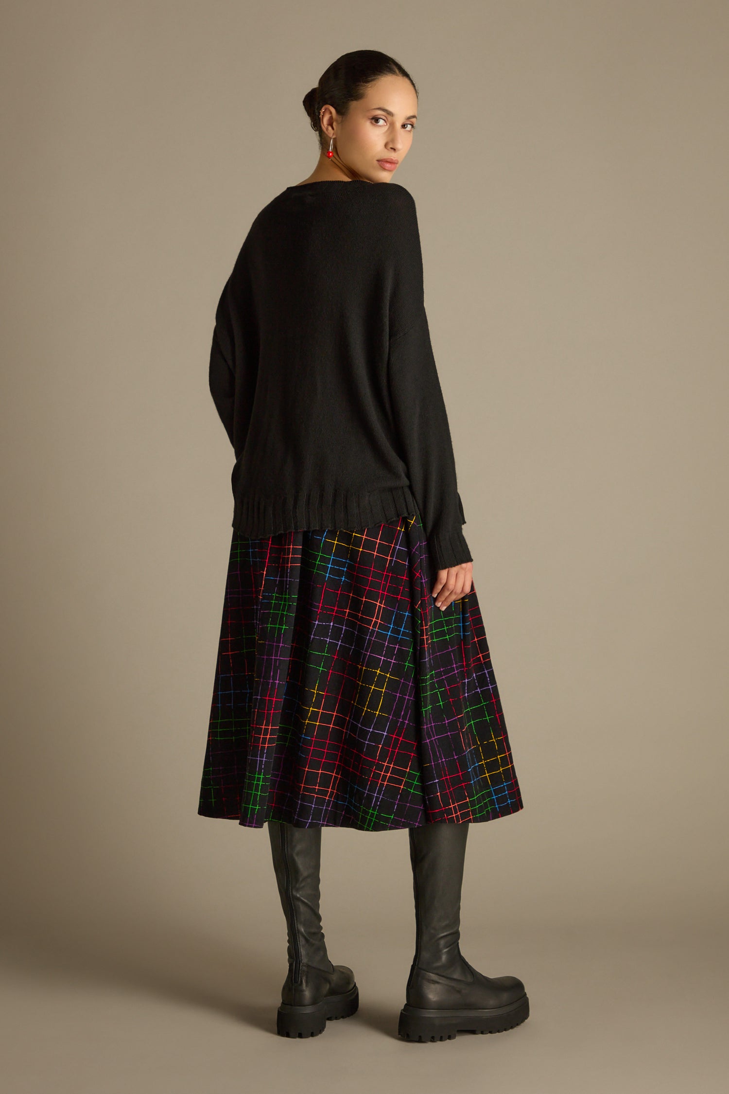 A person wearing a Merino Blend Crop Jumper, plaid skirt, and black boots is standing against a plain background, facing slightly away.