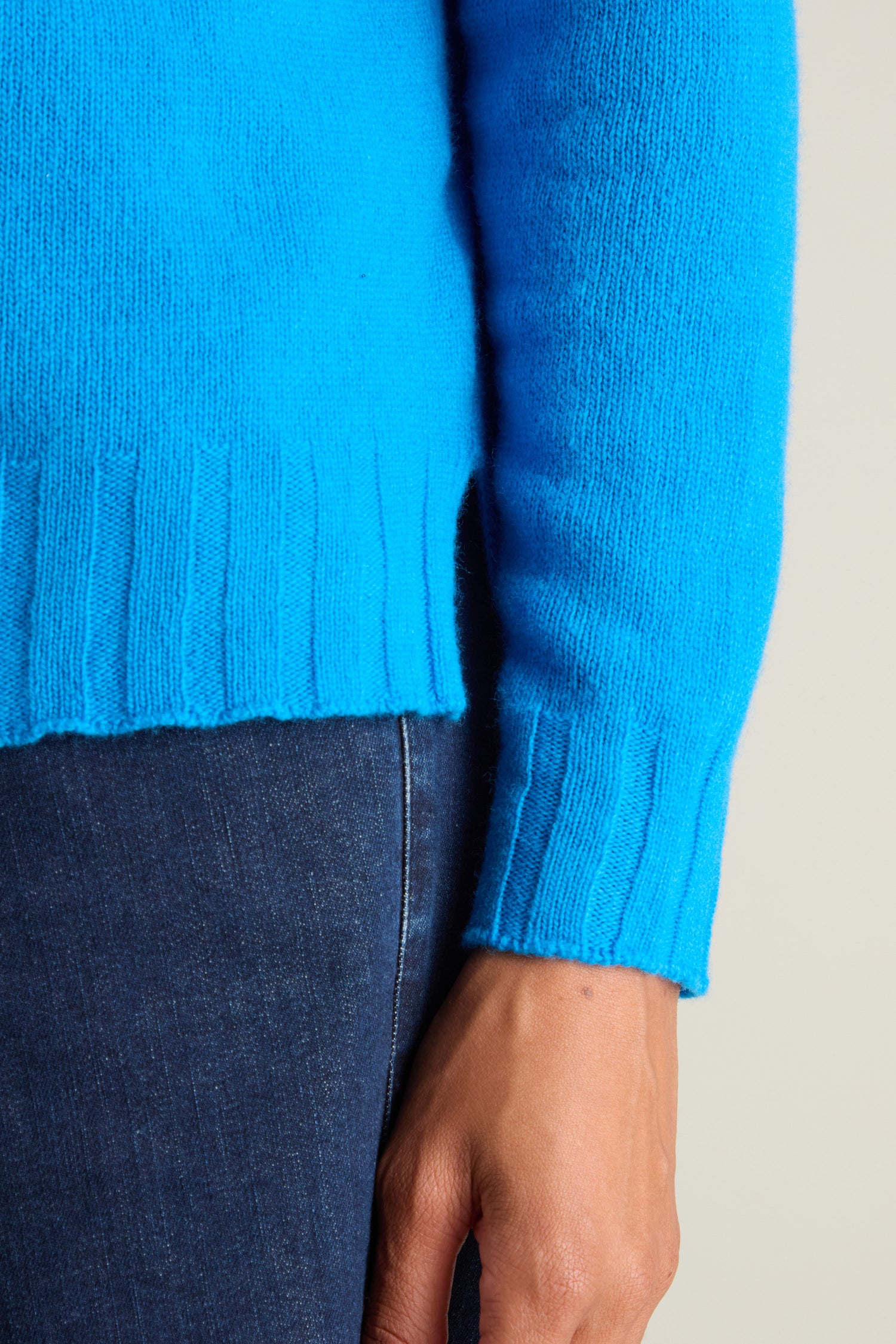 Close-up of an individual wearing a bright blue Cashmere Blend Crop Jumper with ribbed edges and dark blue jeans. The person's arm is relaxed, with their hand partially visible.