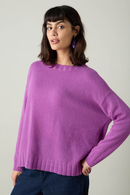 A person in a lively, purple Merino Wool Crop Jumper strikes a pose with one hand on their hip against a plain backdrop.