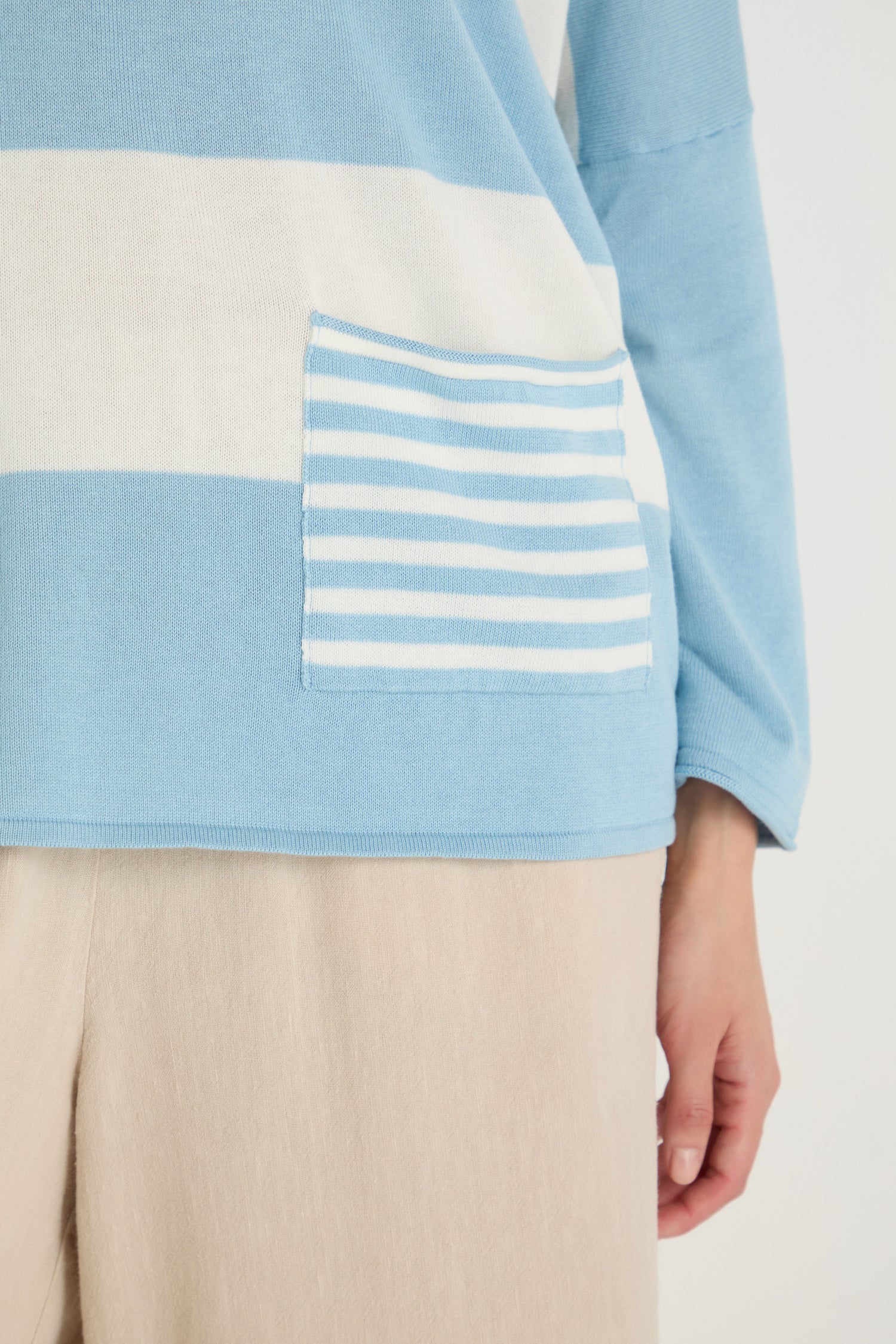 A person wearing beige pants and the Stripe Pocket Knit Top—a blue and white striped knit with a small striped front pocket and a relaxed, boxy fit.