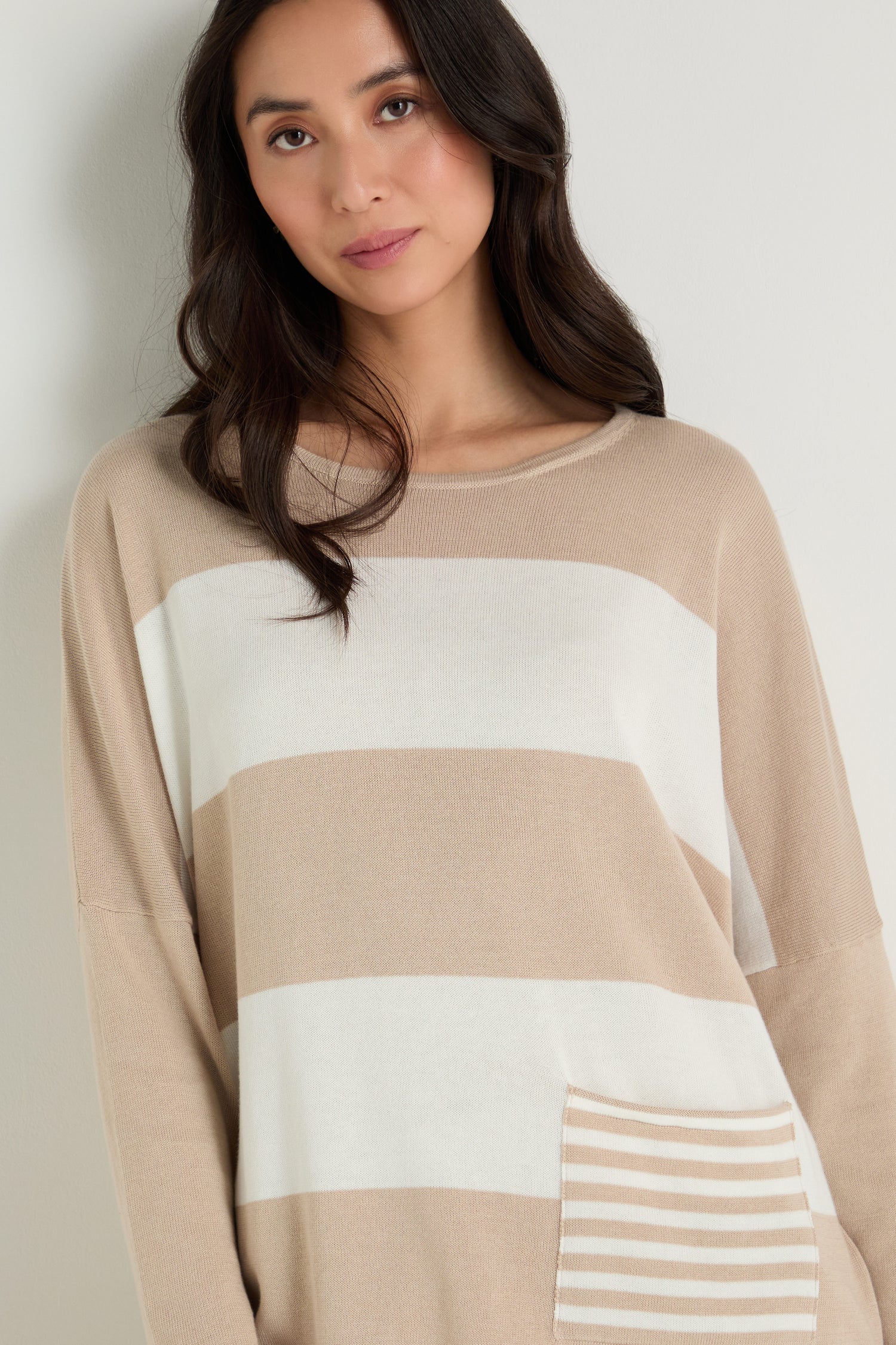A woman with long dark hair wears the Stripe Pocket Knit Top, a relaxed, boxy striped top with a small front pocket, standing against a light background.