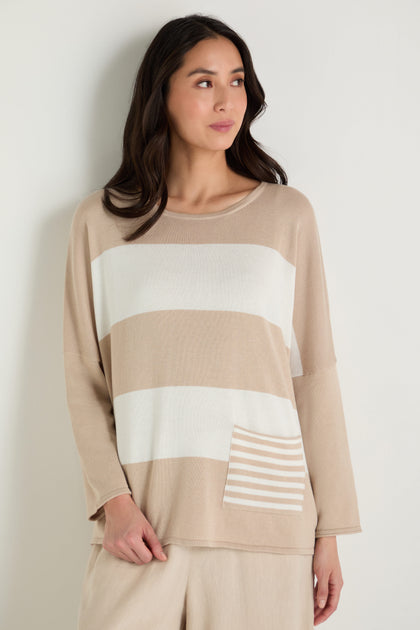 A woman models the Stripe Pocket Knit Top, featuring beige and white stripes, a striped pocket, and a relaxed boxy fit in soft modal cotton, standing against a plain light background.