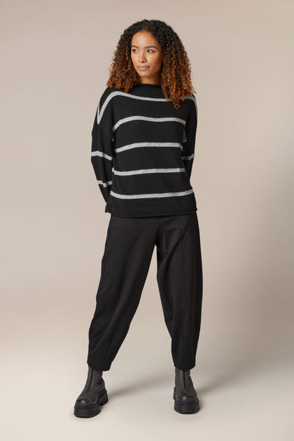 A model wearing a Plaited Stripe Sweater and black trousers with a metallic sheen.
