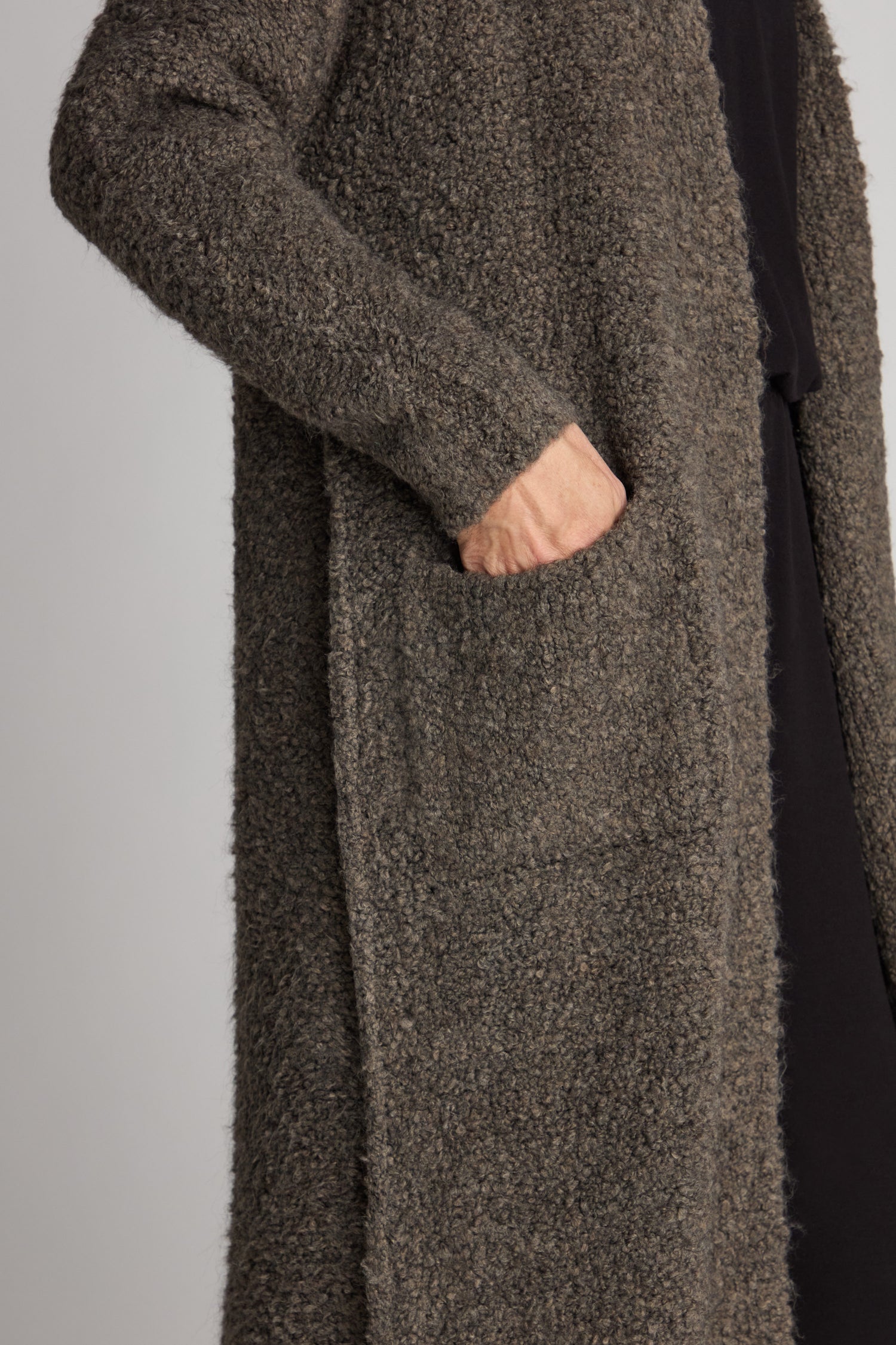 A person wearing the Boucle Knit Long Cardi with their hand in a side pocket, embodying the cozy charm of its textured gray design.