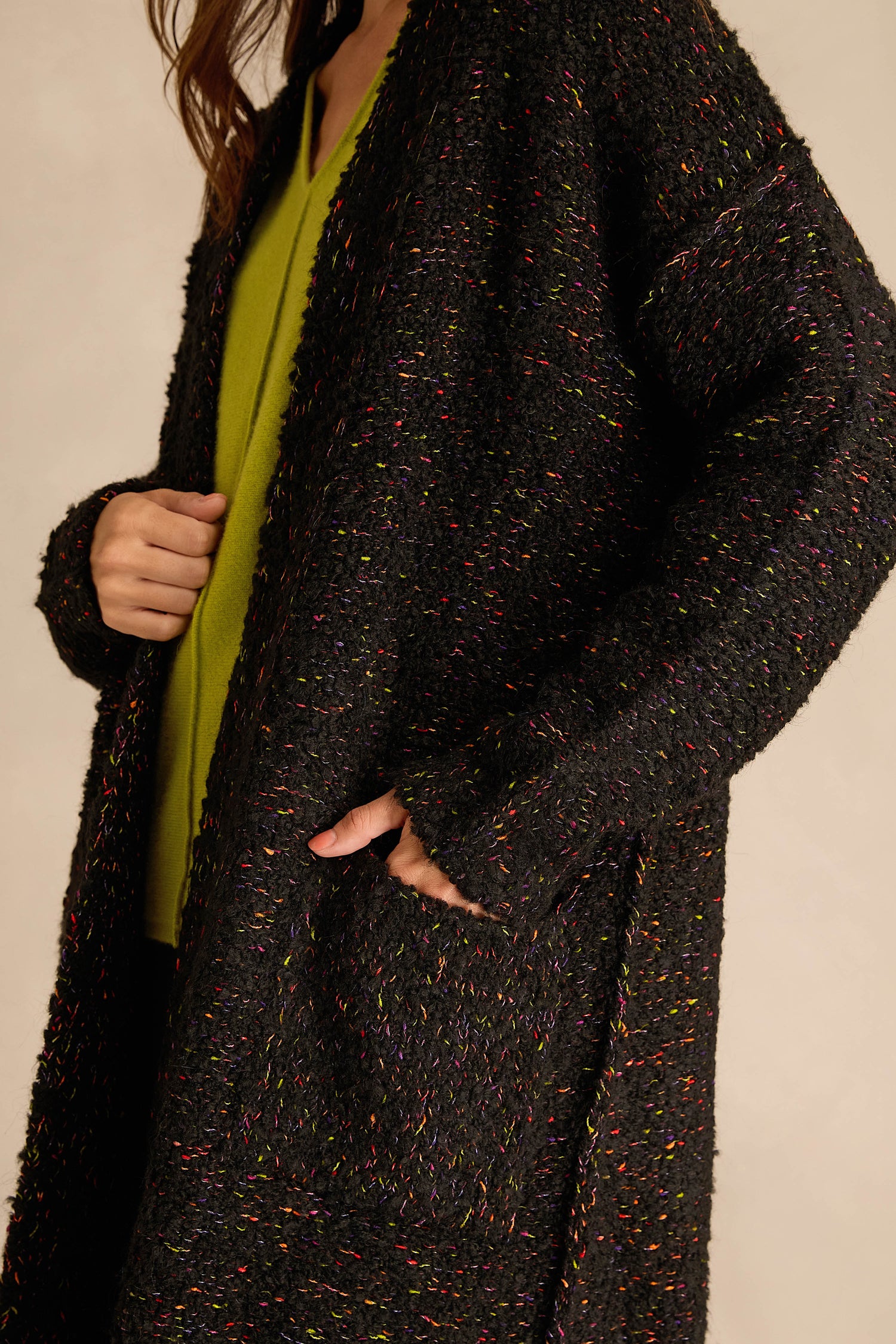 A person wearing the Black Boucle Knit Long Line Speckle Cardi over a green top, with one hand holding the cardigan and the other in a pocket.