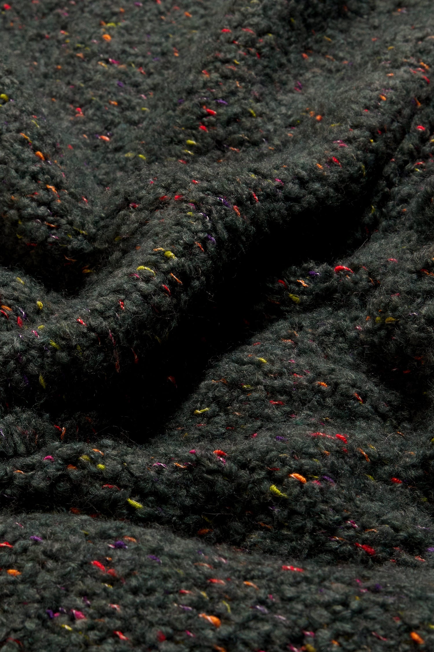Close-up of the Forest Boucle Knit Long Line Speckle Cardi, featuring a dark, textured boucle knit with colorful specks throughout, highlighting its detailed knit patterns and soft folds.