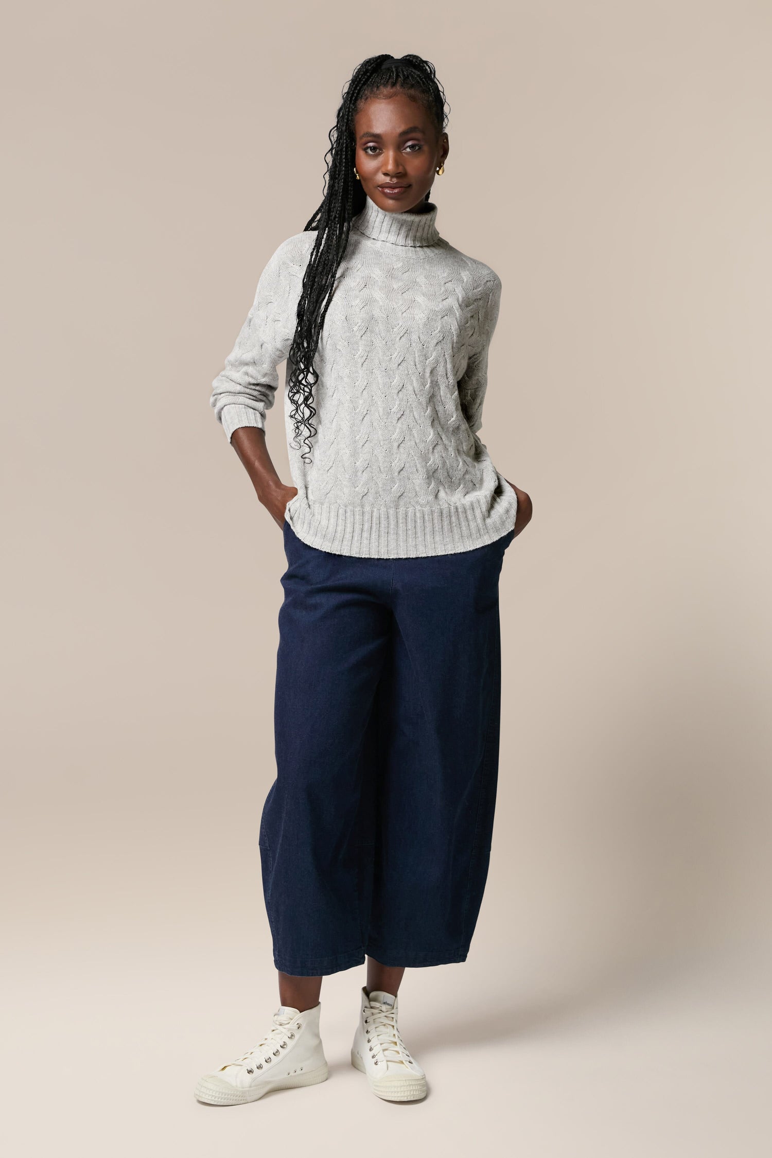 A woman wearing a white cable knit jumper and navy culottes.